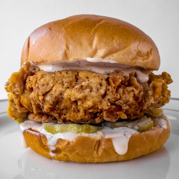 a fried chicken sandwich on a bun with mayonnaise drizzled over it