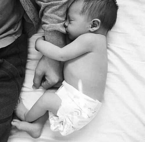 a black and white photo of a baby sleeping next to an adult who is holding it's head