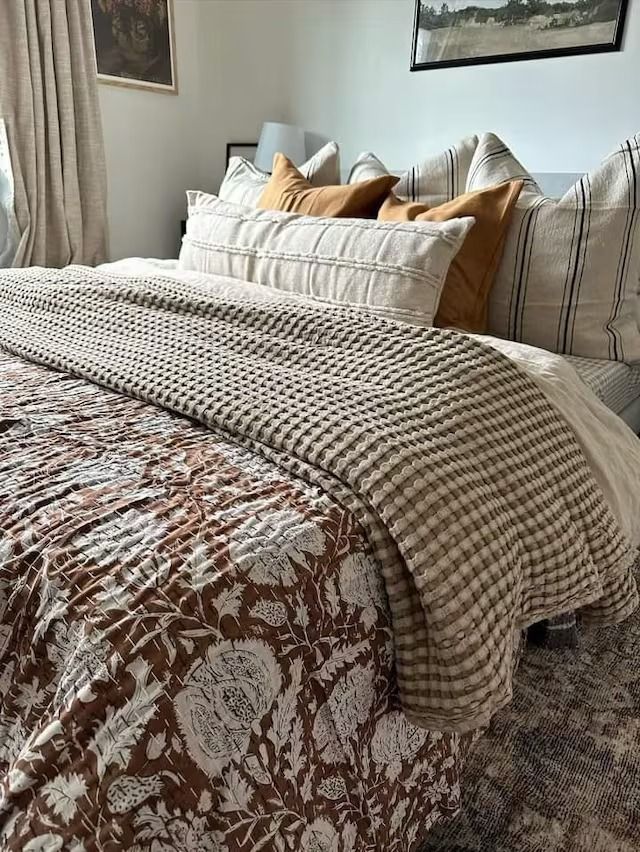 a bed sitting in a bedroom next to a window filled with pillows and blankets on top of it