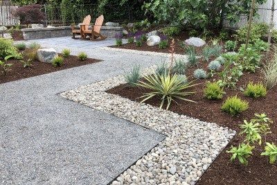 a garden with gravel, rocks and plants in the foreground is an outdoor seating area