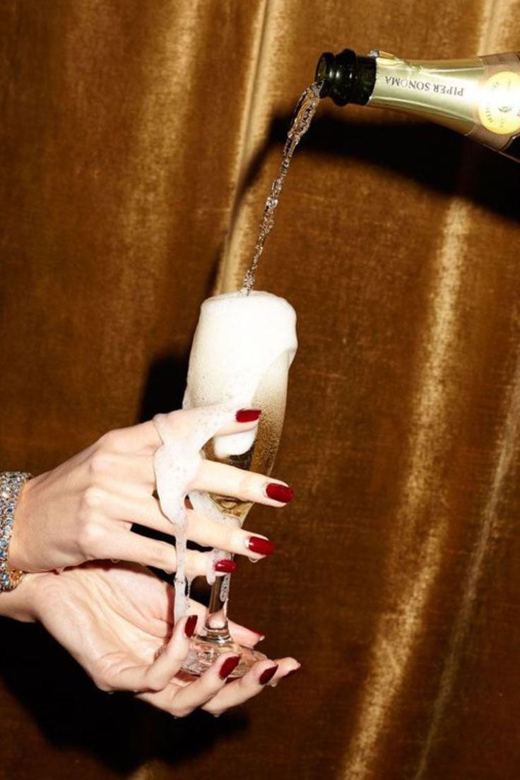 a woman pouring champagne into a glass with her hand and red nail polish on it