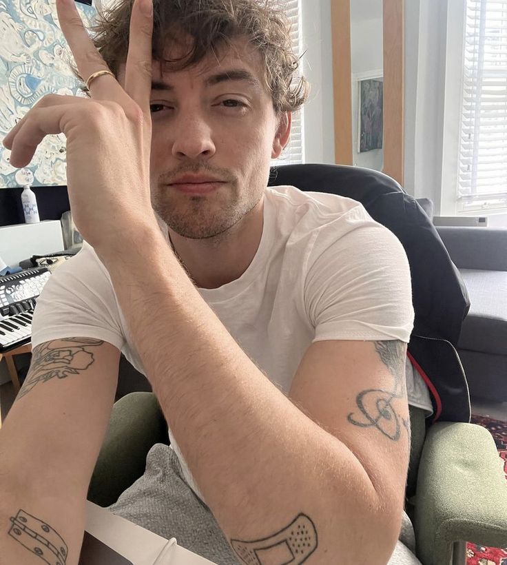 a man sitting in a chair holding his hand up to the camera and making a peace sign