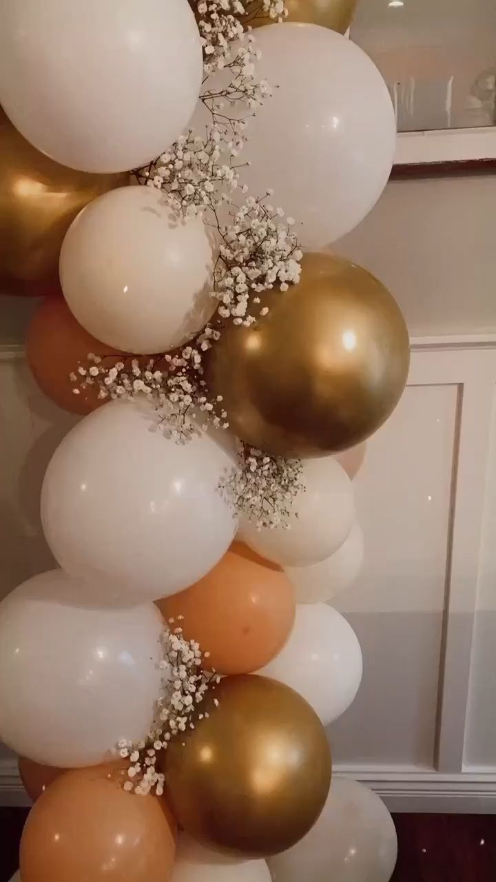 a bunch of balloons that are hanging from a wall with some white and gold balloons