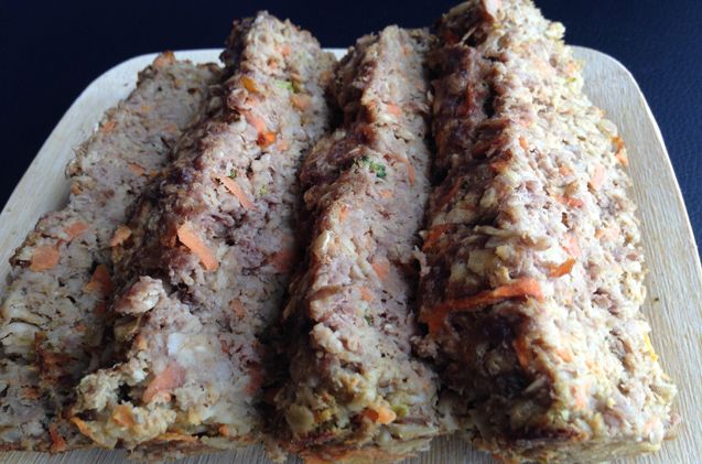 sliced meatloaf sitting on top of a cutting board with carrots and other toppings