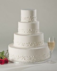 a three tiered white wedding cake next to a glass of wine