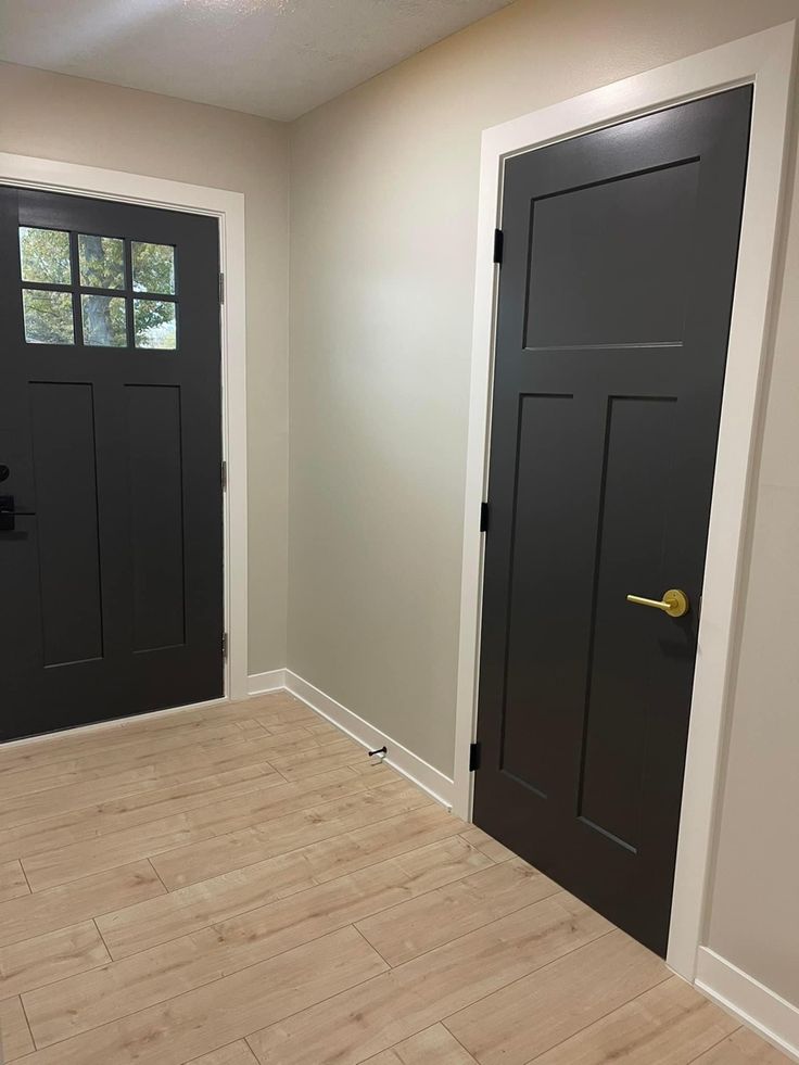 an empty room with two black doors and wood flooring on the side of the room