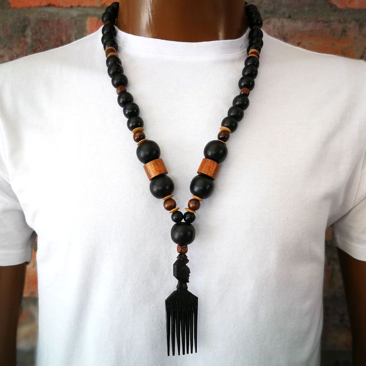 Wood bead necklace with a hand-carved African Wooden Comb  pendant. The African Wood Comb is not just an accessory but a cultural icon. ~  BEAD LENGTH ~ 28" - 71cm ~ D E T A I L S ~ ~  14mm black rustic wood beads ~  20mm black rustic wood beads ~  dark brown wood beads ~  African wood comb pendant ~  pendant - 3 1/2"  (9cm) ~  the pendant is hand carved so it  .  may differ slightly from the picture ~  lobster clasp ~  handmade ~ S H I P P I N G ~ Please see the Announcement on our shop Male African Necklace, Traditional Adjustable Necklace With Wooden Beads, Traditional Adjustable Black Bead Necklaces, Traditional Brown Carved Jewelry, Brown Jewelry With Black Beads For Festival, Festival Brown Jewelry With Black Beads, Traditional Carved Necklaces For Festival, Traditional Carved Adjustable Beaded Necklaces, Traditional Adjustable Carved Beaded Necklaces