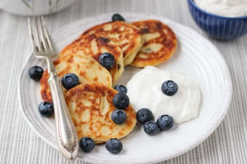 pancakes with blueberries and whipped cream are on a white plate next to a fork