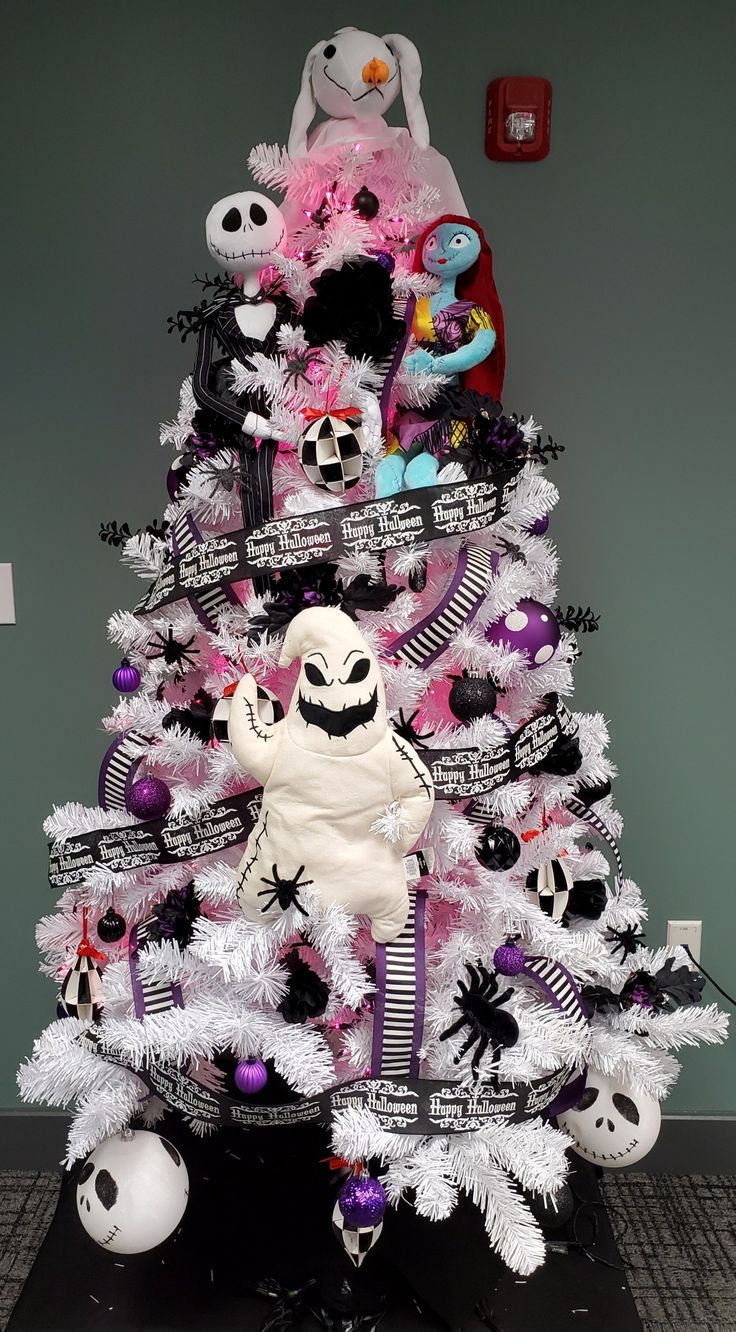 a white christmas tree decorated with black and pink ornaments, skulls, and other decorations