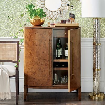 a wooden cabinet with wine glasses and bottles on it in front of a green wallpapered wall