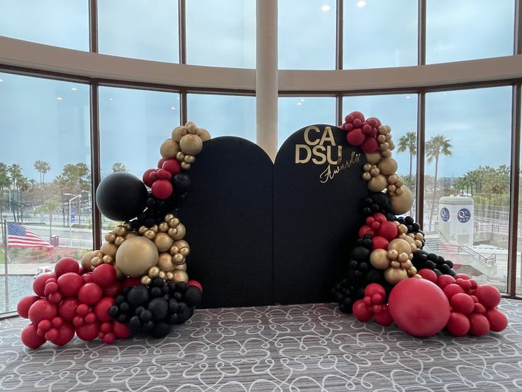 the balloon arch is decorated with red, black and gold balloons in front of large windows