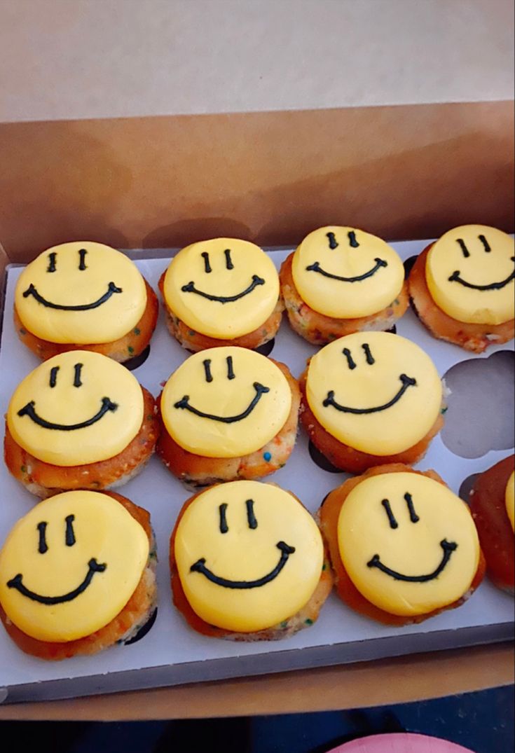 a box filled with lots of yellow cupcakes covered in frosting and smiling faces