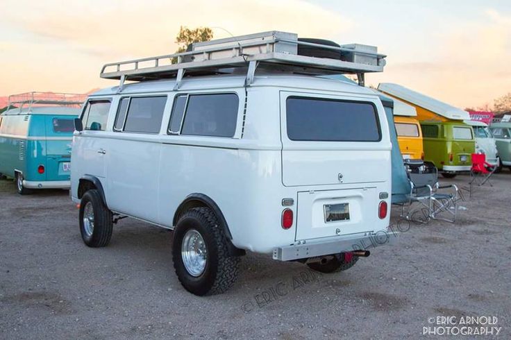 an old white van parked in a parking lot next to other vans and campers