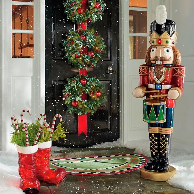 a nutcracker standing in front of a door with a christmas wreath on it