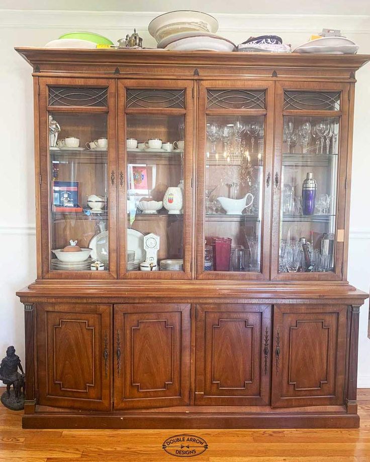 an old china cabinet with glass doors and dishes on it's top, sitting in a living room