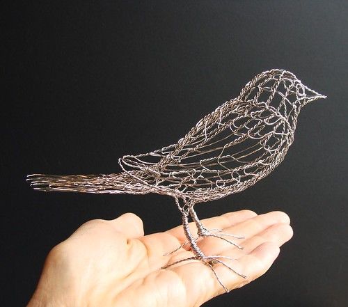 a wire bird sitting on top of someone's hand in front of a black background