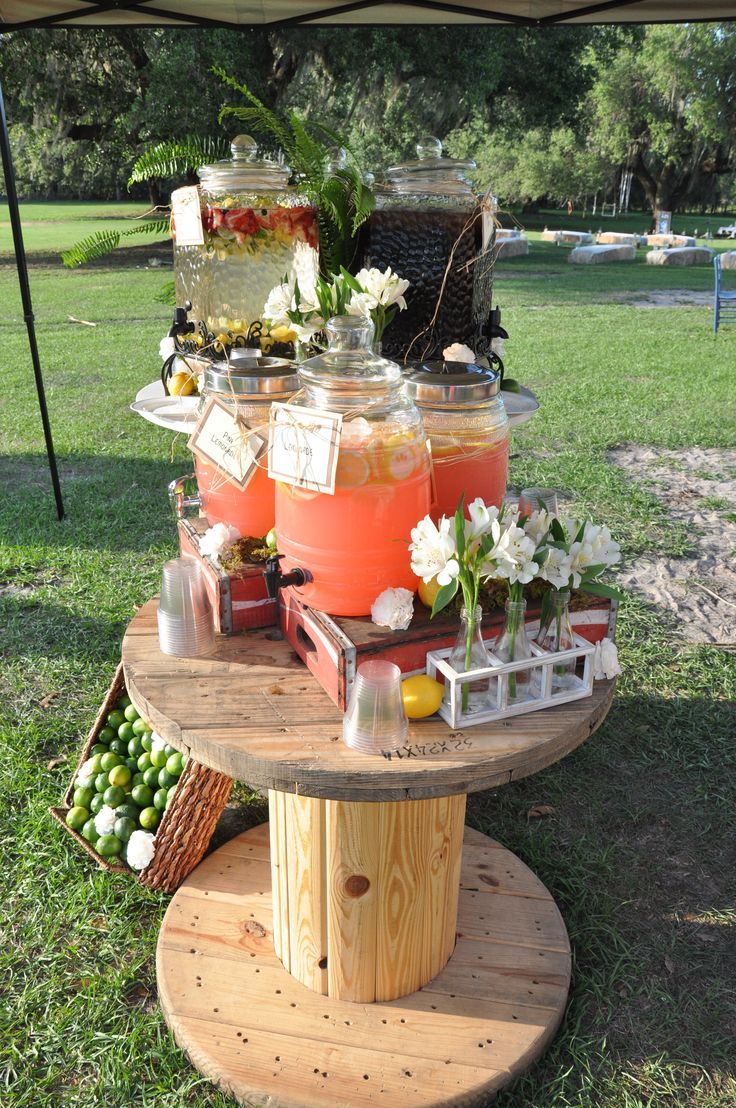 there is a table with drinks on it in the grass and some flowers are around