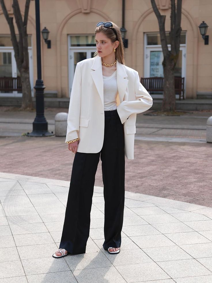 a woman standing in front of a building wearing a white blazer and black pants