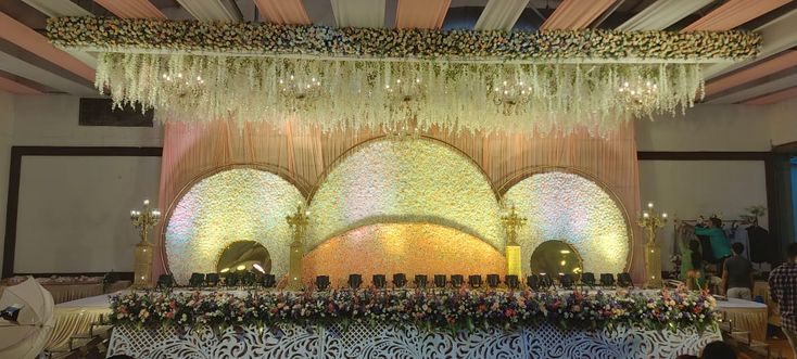 an elaborate stage set up with chandeliers and flowers on the ceiling for a wedding reception