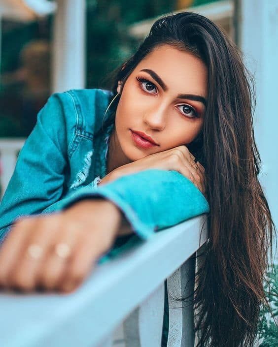 a woman with long hair leaning on a railing looking at the camera while wearing a denim jacket