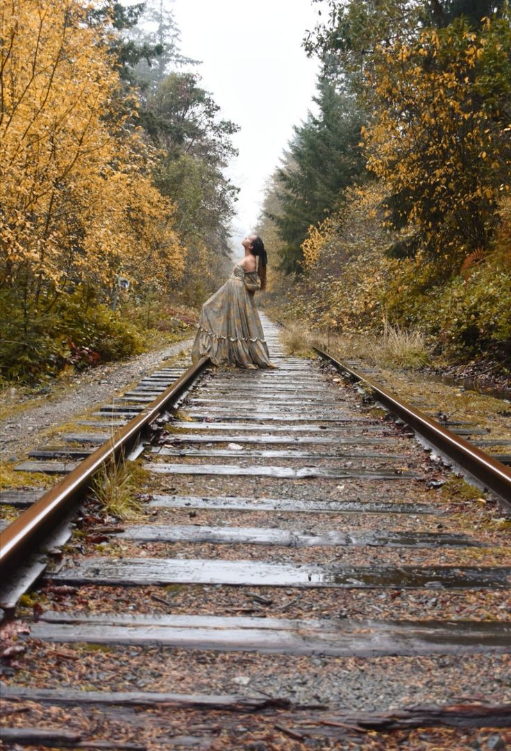 a woman standing on train tracks in the middle of an autumn forest with yellow trees