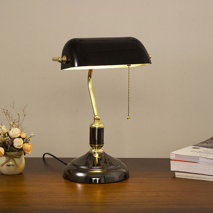 a desk lamp sitting on top of a wooden table next to a vase with flowers