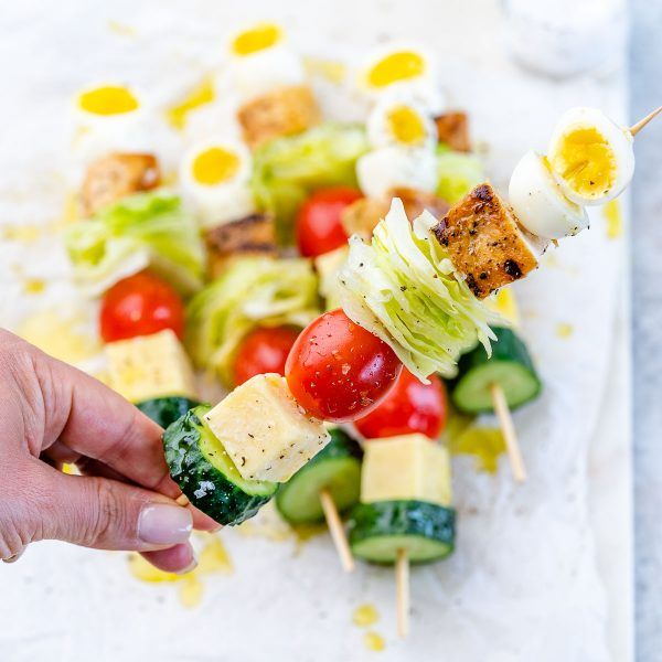 a person holding a skewer of food on a white tray with other foods