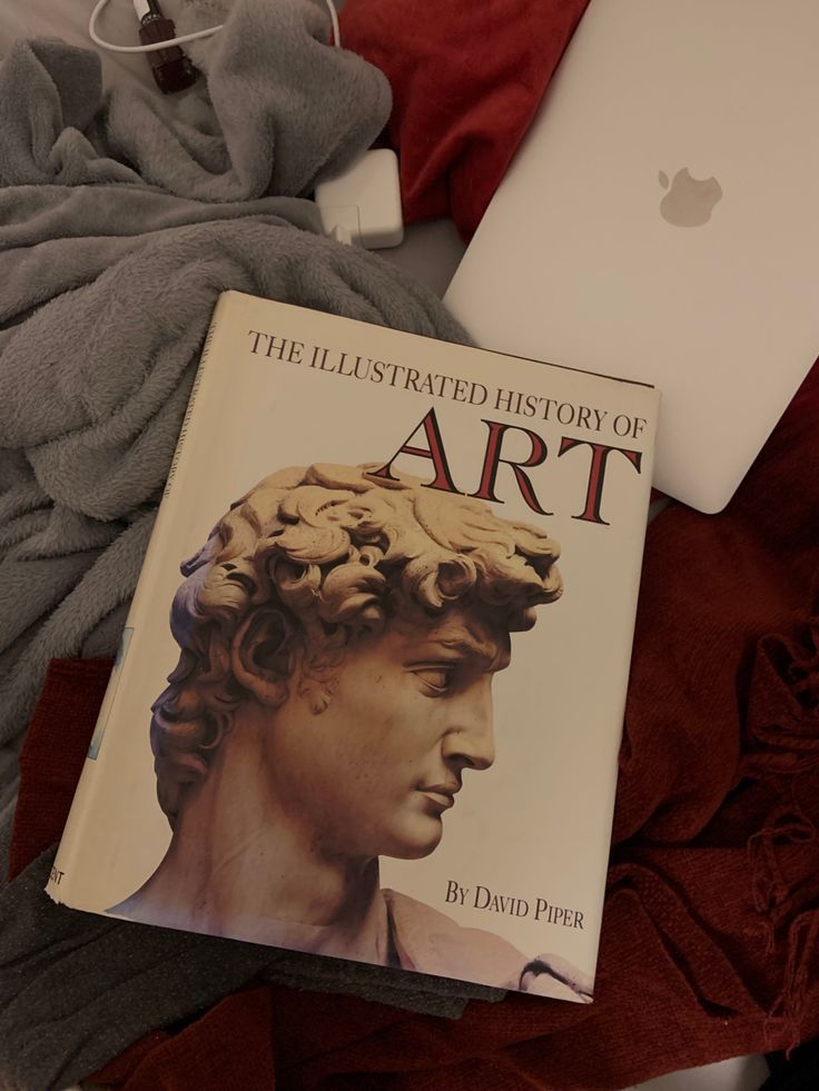 an apple computer sitting on top of a bed next to a book titled the illustrated history of art