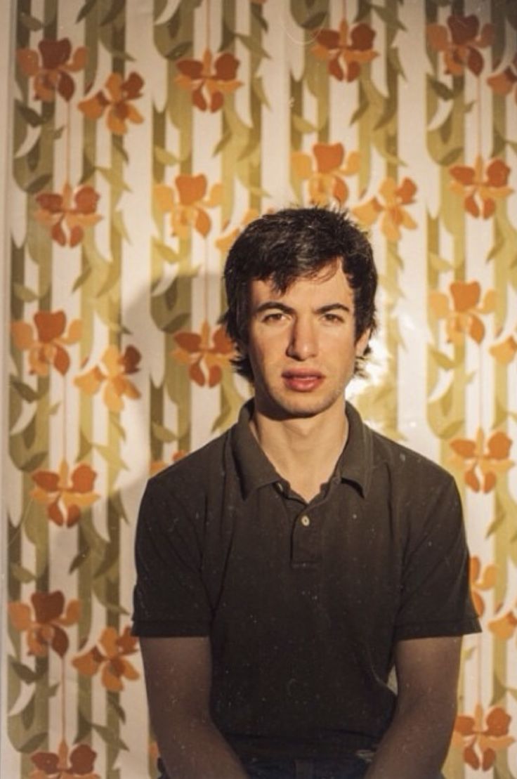 a young man sitting in front of a wall with flowers on it's side