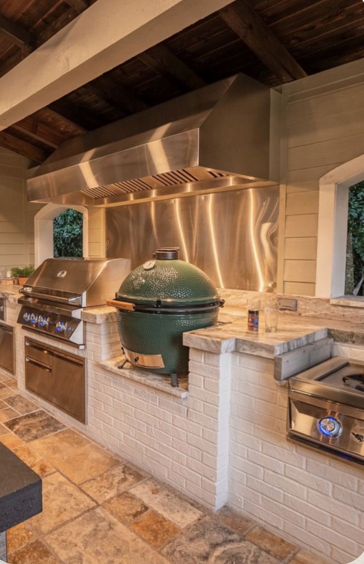 an outdoor kitchen with stainless steel appliances and grills on the outside wall, along with stone flooring