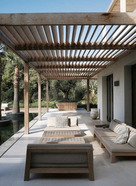 an outdoor living area with couches and tables under a pergolated roof next to a swimming pool