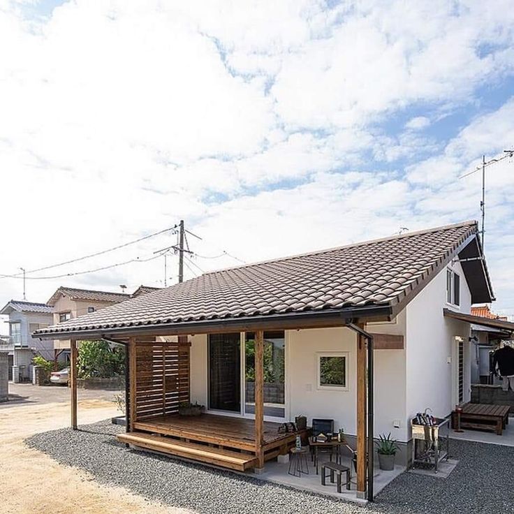 a small white house with a wooden deck in the middle of graveled area next to it