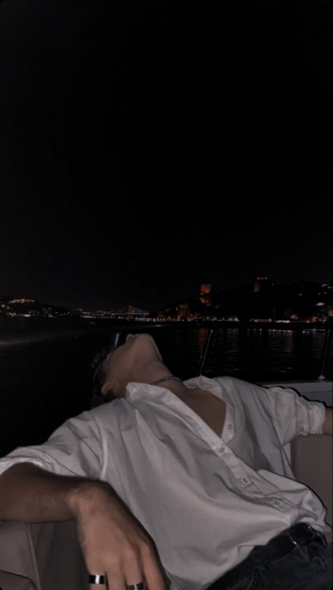 a man laying on the back of a boat in the water at night with his eyes closed