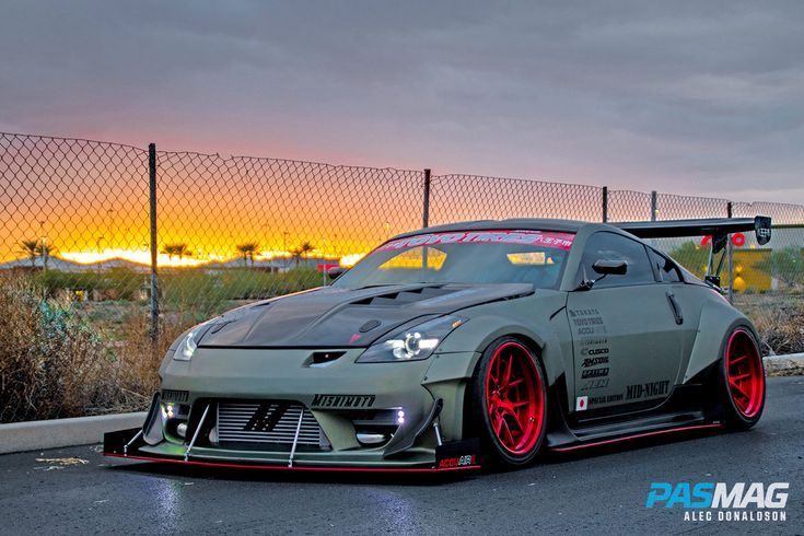 a gray sports car with red rims parked in front of a fence