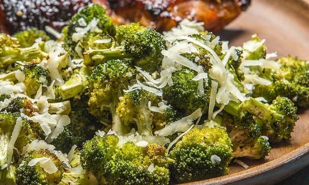 broccoli with shredded parmesan cheese is on a plate next to chicken