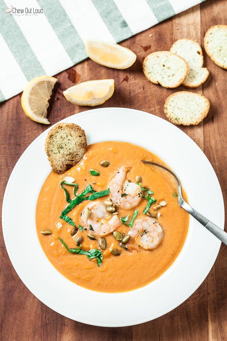 a bowl of soup with shrimp and bread on the side, ready to be eaten