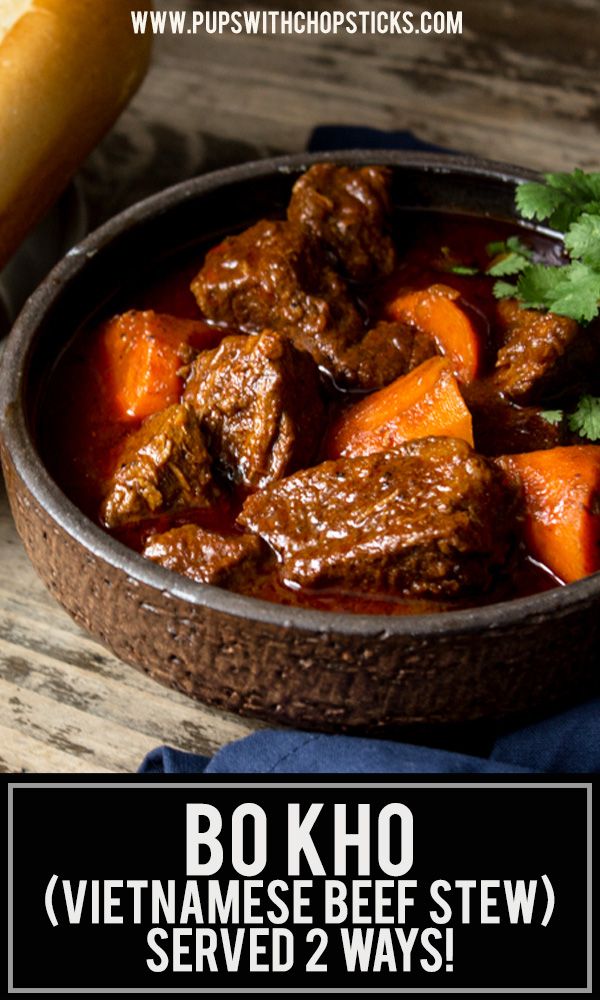 a bowl filled with beef and carrots on top of a wooden table next to bread