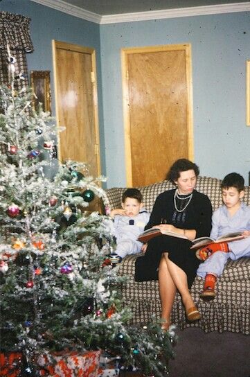 a woman and two boys sitting on a couch with a christmas tree in the background