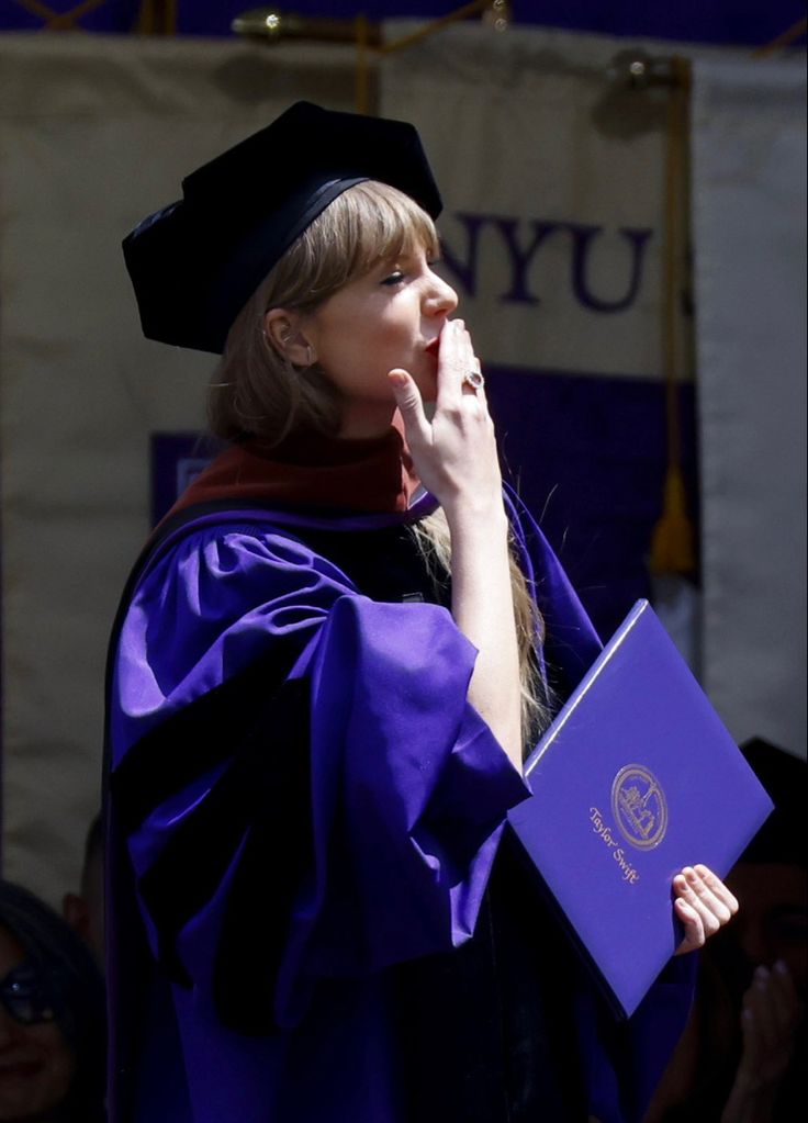 a woman wearing a purple graduation gown and holding a blue folder in her right hand