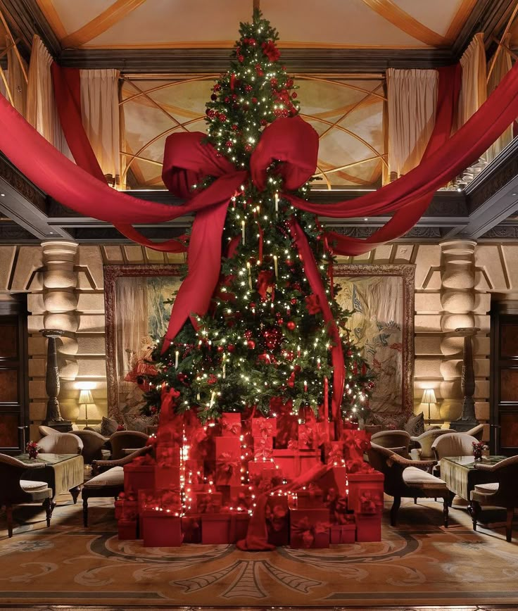 a large christmas tree with red bows and presents under it in a room decorated for the holidays