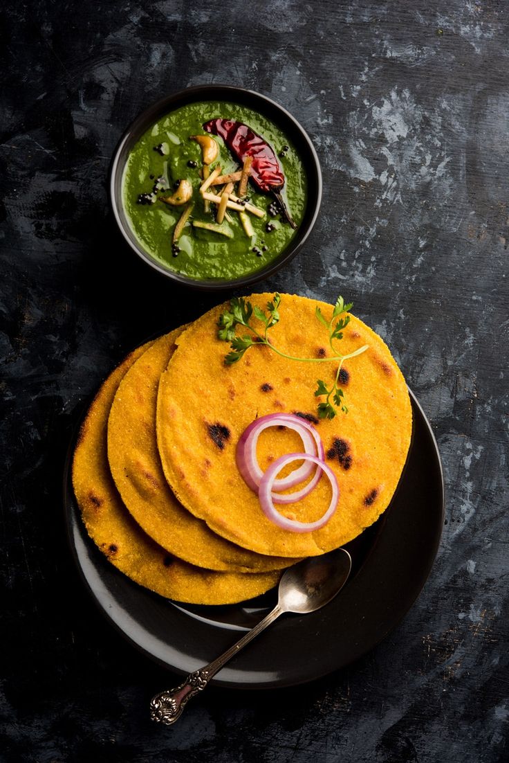 three tortillas with onions and herbs on a black plate next to a spoon