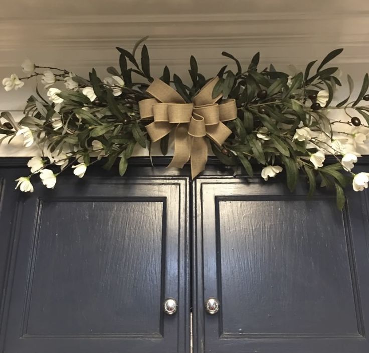 a bow on top of a cabinet with flowers and greenery hanging from the front