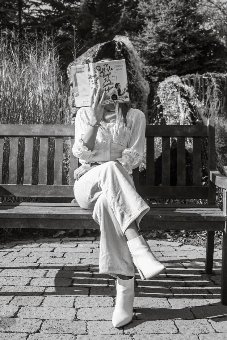 a black and white photo of a woman sitting on a park bench reading a book