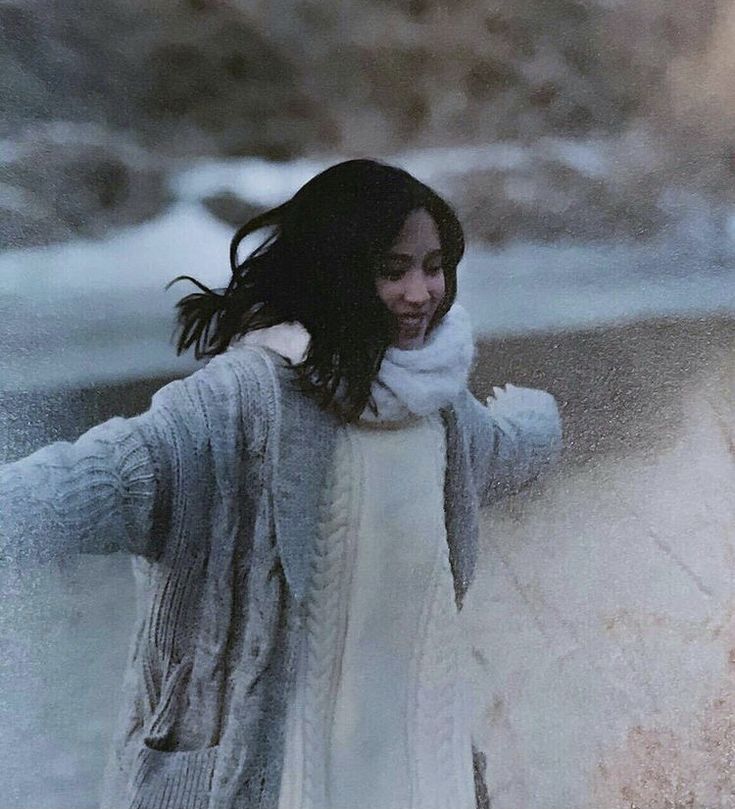 a woman is standing in the snow with her arms spread out and she's wearing a white sweater