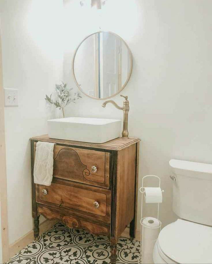 a white toilet sitting next to a wooden cabinet in a bathroom under a mirror and a sink