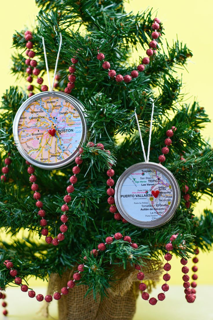 two christmas ornaments hanging from a tree with red berries on the branches and map pins attached to them