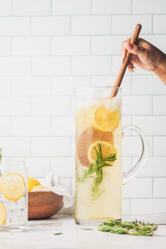 a pitcher filled with lemonade and herbs