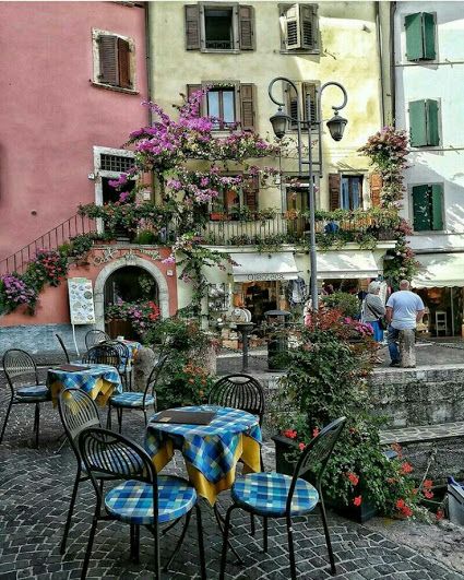 tables and chairs are set up outside in front of buildings with flowers growing on the balconies