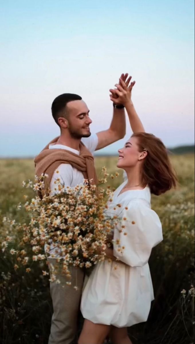 a man and woman standing in a field with flowers holding each other's hands