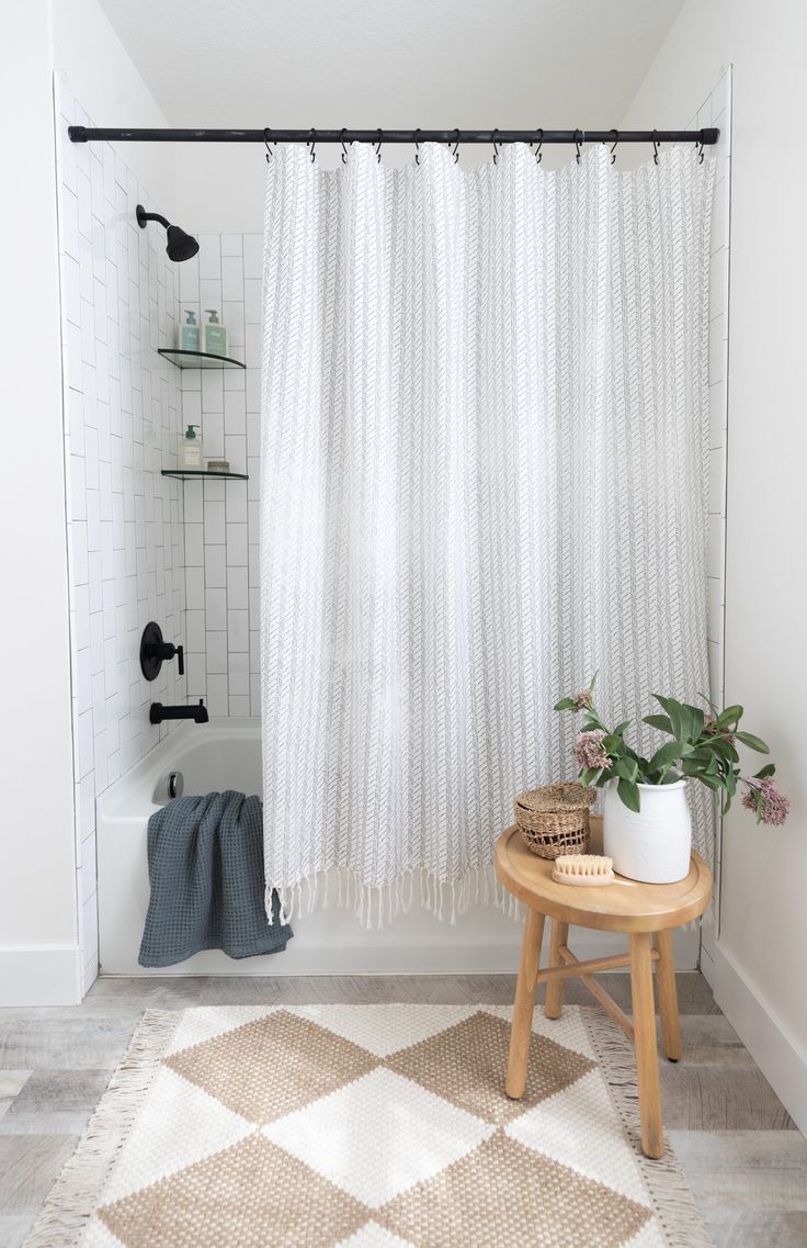 a white shower curtain in a bathroom next to a wooden stool and potted plant